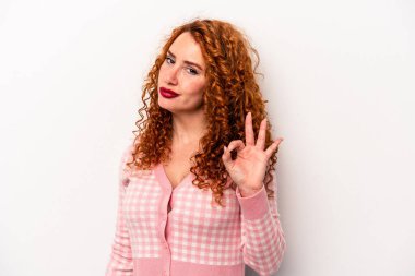 Beyaz arka planda soyutlanmış beyaz tenli genç bir kadın göz kırpıyor ve elleriyle iyi bir jest yapıyor..