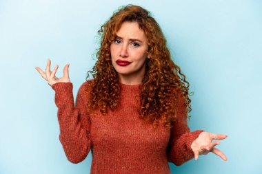 Genç, beyaz, mavi arka planda izole edilmiş bir kadın sorgulama sırasında omuz silkiyor ve şüphe ediyor..