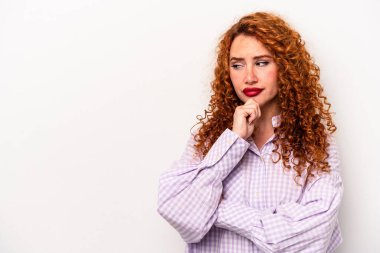 Beyaz arka planda soyutlanmış beyaz tenli genç bir kadın şüpheli ve şüpheci bir ifadeyle yana bakıyor..