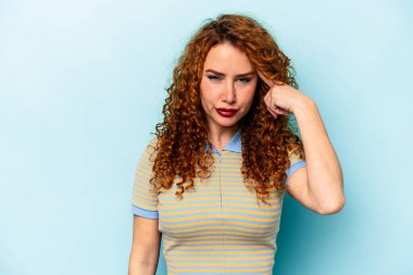 Genç, beyaz, mavi arka planda izole edilmiş bir kadın şakağı parmağıyla işaret ediyor, düşünüyor ve bir göreve odaklanıyor..