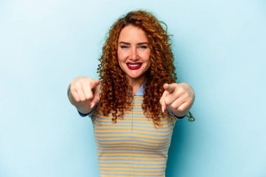 Genç, beyaz, mavi arka planda izole edilmiş bir kadın. Önü işaret eden neşeli gülümsemeler..