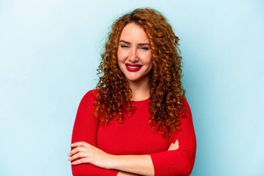 Mavi arka planda kendini güvende hisseden, kararlılıkla kollarını kavuşturan genç beyaz bir kadın..