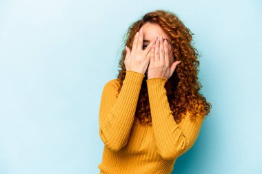 Genç, beyaz, mavi arka planda izole edilmiş bir kadın parmaklarıyla gözünü kırp korkmuş ve gergin..