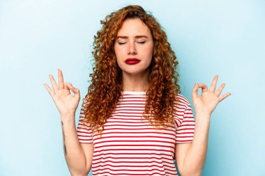 Mavi arka planda izole edilmiş genç kızıl saçlı kadın yoğun bir günün ardından rahatlıyor, yoga yapıyor..