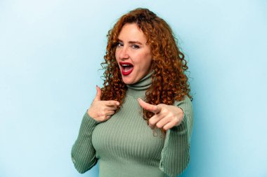 Genç, beyaz, mavi arka planda izole edilmiş, parmaklarıyla ön tarafı gösteren bir kadın..