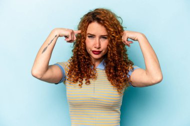 Mavi arka planda izole edilmiş genç beyaz kadın bir işe odaklanmış, işaret parmaklarını işaret ediyor..