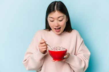 Genç Asyalı bir kadın mavi arka planda bir kase mısır gevreği tutuyor.