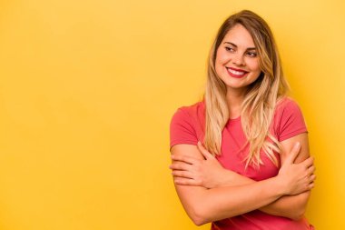 Sarı arka planda izole edilmiş genç beyaz kadın kollarını kavuşturarak gülümsüyor..