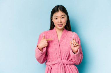 Mavi arka planda jilet tutan Asyalı genç bir kadın gömleğin fotokopi alanını elle işaret ediyor, gururlu ve kendinden emin.