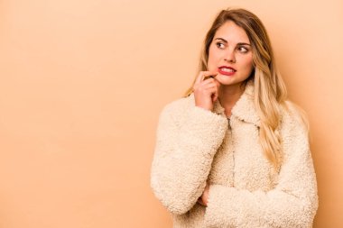 Beyazlı genç bir kadın bej arka planda izole edilmiş şüpheli ve şüpheci bir ifadeyle yana bakıyor..