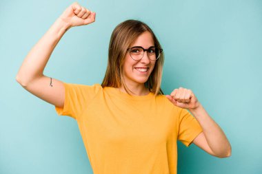 Mavi arka planda izole edilmiş genç beyaz kadın özel bir günü kutluyor, atlıyor ve enerjiyle kollarını kaldırıyor..