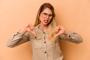 Beyazlı genç bir kadın bej arka planda izole edilmiş. Baş parmağını aşağı gösteriyor ve hoşlanmadığını ifade ediyor..