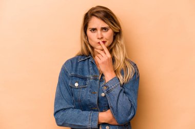 Beyaz tenli genç bir kadın bej arka planda izole edilmiş düşünüyor ve yukarı bakıyor, yansıtıyor, düşünüyor, hayal kuruyor..