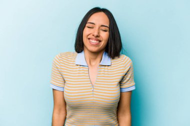 Mavi arka planda izole edilmiş genç İspanyol kadın gülüyor ve gözlerini kapıyor, rahatlamış ve mutlu hissediyor..