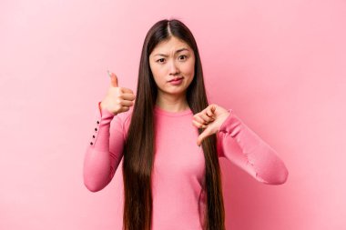 Pembe arka planda izole edilmiş genç Çinli bir kadın baş parmağını kaldırıyor. Zor bir seçim konsepti.