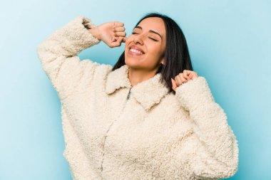 Mavi arka planda izole edilmiş genç İspanyol kadın özel bir günü kutluyor, atlıyor ve enerjiyle kollarını kaldırıyor..