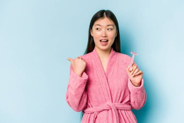 Elinde jilet tutan Asyalı genç bir kadın mavi arka plan noktalarına izole edilmiş başparmak uzakta, gülüyor ve kaygısız..