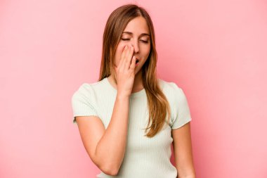 Pembe arka planda izole edilmiş genç beyaz kadın esniyor. Ağzı eliyle kapatan yorgun bir hareket sergiliyor..