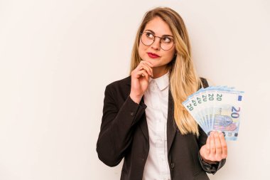 Beyaz arka planda soyutlanmış, şüpheli ve şüpheci bir ifadeyle yan bakan beyaz banknotlar tutan genç beyaz bir kadın..