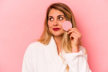 Pembe arka planda yüz süngeri tutan beyaz bir kadın var.