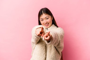 Pembe arka planda izole edilmiş genç Çinli kadın parmaklarıyla ön tarafı işaret ediyor..