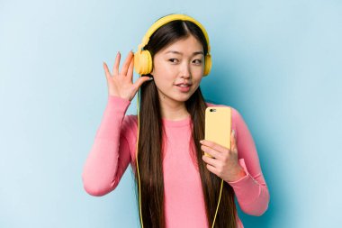 Mavi arka planda müzik dinleyen Asyalı genç bir kadın bir dedikoduyu dinlemeye çalışıyor..