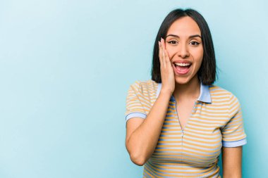 Mavi arka planda izole edilmiş genç İspanyol kadın yüksek sesle bağırıyor, gözleri açık ve elleri gergin tutuyor..