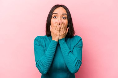 Pembe arka planda izole edilmiş genç İspanyol kadın şok olmuş, ağzı ellerle kaplanmış, yeni bir şey keşfetmeye hevesli..