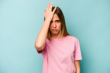 Kafkasyalı genç bir kadın mavi arka planda izole edilmiş bir şekilde bir şeyi unutuyor. Alnına avuç içi ve gözlerini kapayarak vuruyor..