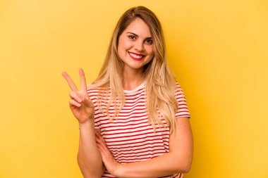 Sarı arka planda izole edilmiş genç beyaz kadın iki numarayı parmaklarıyla gösteriyor..