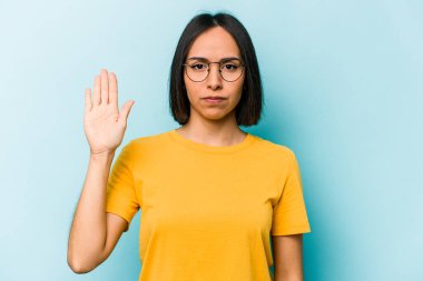 Mavi arka planda izole edilmiş genç İspanyol kadın gülümseyerek beş numarayı parmaklarıyla gösteriyor..