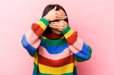 Pembe arka planda izole edilmiş genç İspanyol kadın kameraya parmaklarıyla göz kırpıyor, yüzünü kapatmaktan utanıyor..