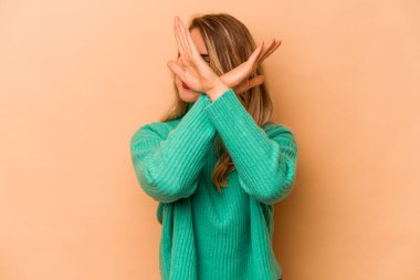 Beyazlı genç bir kadın bej arka planda izole edilmiş iki kolu çapraz tutuyor, inkar kavramı.