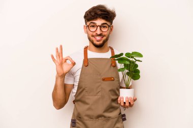 Genç bahçıvan İspanyol bir bitki tutuyor. Beyaz arka planda izole edilmiş. Neşeli ve kendinden emin..