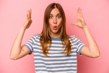 Pembe arka planda izole genç beyaz kadın zaferi ya da başarıyı kutluyor, şaşırıyor ve şok oluyor..