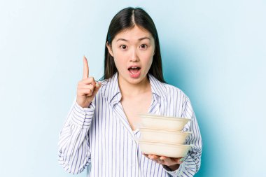 Elinde saklama kabı olan Asyalı genç bir kadın mavi arka planda izole edilmiş bir şekilde. Bir fikri var, ilham verici bir kavram..