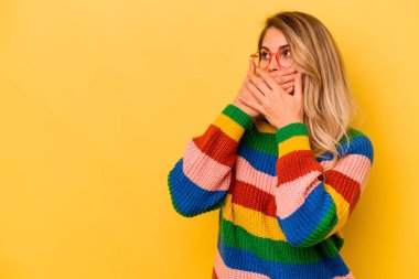 Genç beyaz kadın, sarı arka planda izole edilmiş. Düşünceli bir şekilde, ağzı elle kapatılmış bir fotokopi odasına bakıyor..