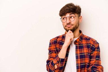 Beyaz arka planda izole edilmiş genç bir İspanyol şüpheli ve şüpheci bir ifadeyle yana bakıyor..