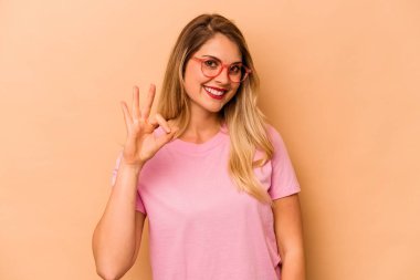 Beyaz tenli genç bir kadın bej arka planda izole edilmiş neşeli ve kendinden emin..