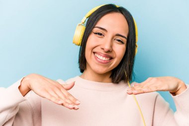 Genç İspanyol kadın mavi arka planda izole edilmiş müzik dinliyor.