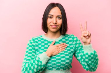 Genç İspanyol kadın pembe arka planda izole edilmiş yemin ediyor, elini göğsüne koyuyor..