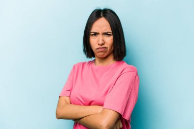 Young hispanic woman isolated on blue background frowning face in displeasure, keeps arms folded. clipart