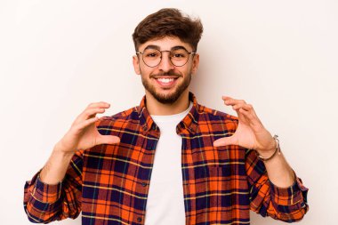 Beyaz arka planda izole edilmiş genç İspanyol bir adam avuçlarıyla bir şey tutuyor ve kameraya sunuyor..