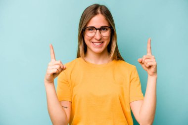 Mavi arka planda izole edilmiş genç beyaz kadın iki parmağı da boş bir alan gösteriyor..