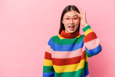 Pembe arka planda izole edilmiş genç Çinli kadın yüksek sesle bağırıyor, gözleri açık ve elleri gergin tutuyor..