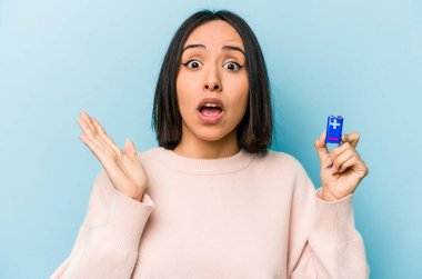 Mavi arka planda pil tutan genç İspanyol kadın şaşırdı ve şok oldu..