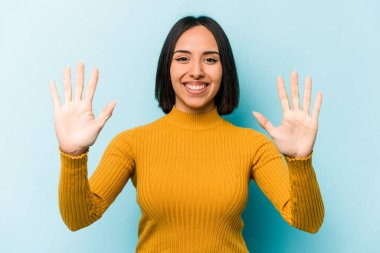 Mavi arka planda izole edilmiş genç İspanyol kadın on numarayı elleriyle gösteriyor..