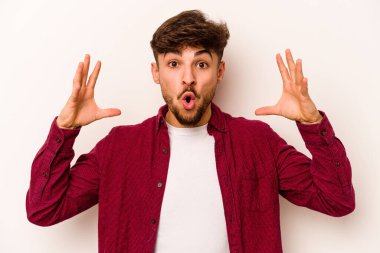 Latin kökenli genç bir adam zaferi ya da başarıyı kutlarken beyaz arka planda mahsur kaldı. Şaşırdı ve şok oldu..