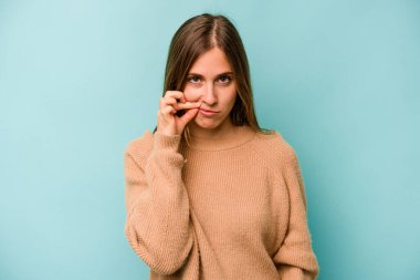 Mavi arka planda izole edilmiş genç beyaz kadın parmakları dudaklarında bir sır saklıyor..