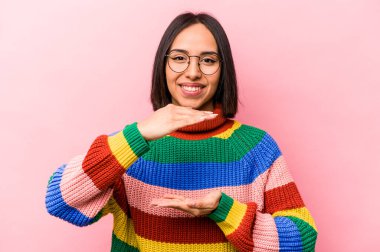 Pembe arka planda izole edilmiş genç İspanyol kadın iki eliyle bir şey tutuyor, ürün sunumu..